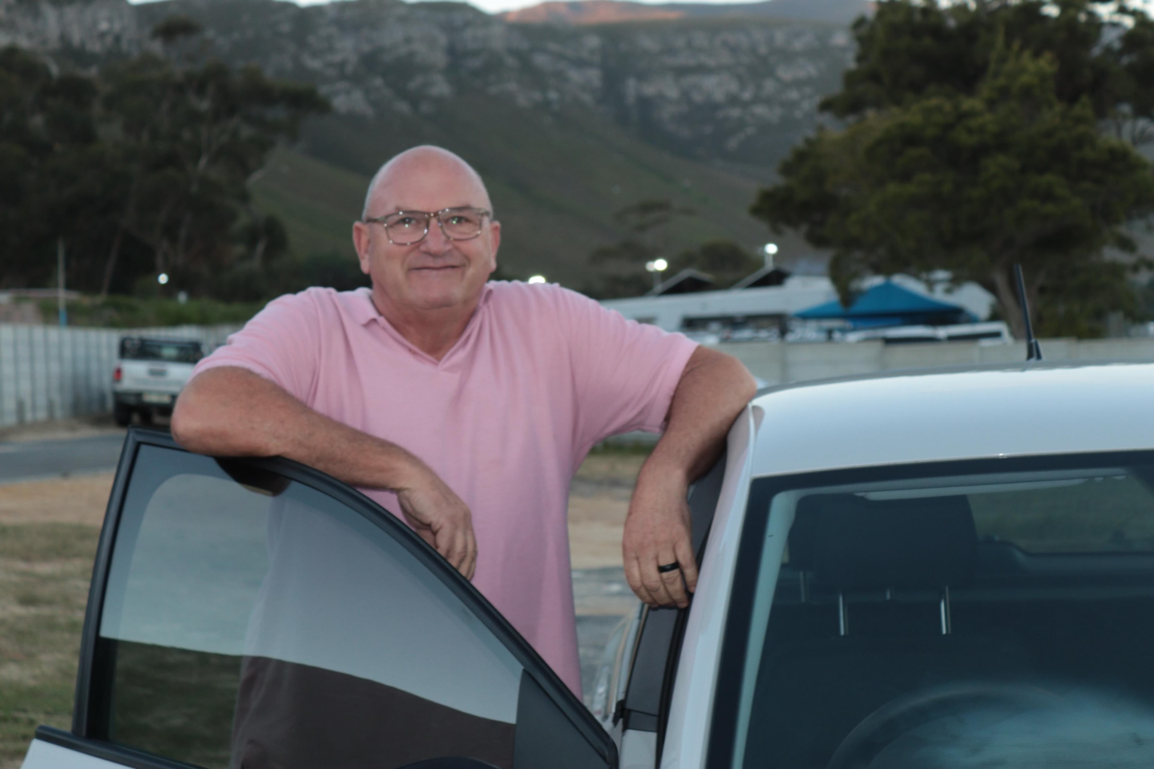 Your instructor leaning on the door of the white VW Polo, Hermanus mountains behind him at dusk